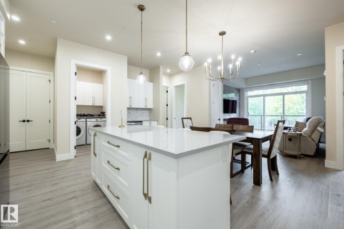 Kitchen featuring a center island, light stone countertops, decorative light fixtures, open floor plan, and washing machine and dryer - 7471 May Common, Edmonton, AB - Indoor