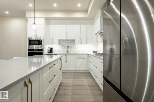 Kitchen with appliances with stainless steel finishes, white cabinets, decorative backsplash, light stone counters, and decorative light fixtures - 7471 May Common, Edmonton, AB - Indoor Photo Showing Kitchen With Upgraded Kitchen