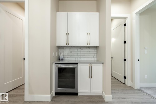 Indoor dry bar featuring wine cooler, white cabinetry, and tasteful backsplash - 7471 May Common, Edmonton, AB - Indoor Photo Showing Other Room