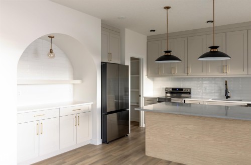 Kitchen with stainless steel appliances, hanging light fixtures, light wood-type flooring, light stone counters, and tasteful backsplash - 163 Starling Way, Fort Saskatchewan, AB - Indoor Photo Showing Kitchen