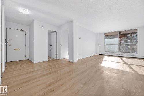 Unfurnished living room with light wood-type flooring, a baseboard radiator, and a textured ceiling - 207 11007 83 Avenue, Edmonton, AB - Indoor Photo Showing Other Room