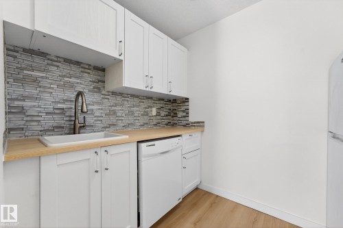 Kitchen with butcher block counters, white appliances, decorative backsplash, light wood-style flooring, and white cabinets - 207 11007 83 Avenue, Edmonton, AB - Indoor