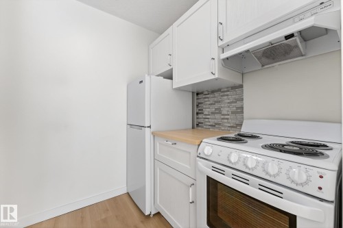 Kitchen featuring white appliances, white cabinetry, backsplash, light wood-type flooring, and butcher block counters - 207 11007 83 Avenue, Edmonton, AB - Indoor Photo Showing Kitchen