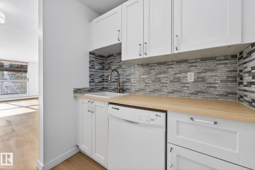 Kitchen with dishwasher, wood counters, white cabinets, and light wood finished floors - 207 11007 83 Avenue, Edmonton, AB - Indoor Photo Showing Kitchen