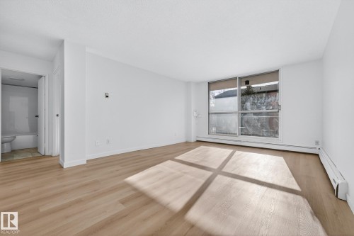 Empty room with light wood-style floors, a baseboard radiator, and baseboard heating - 207 11007 83 Avenue, Edmonton, AB - Indoor
