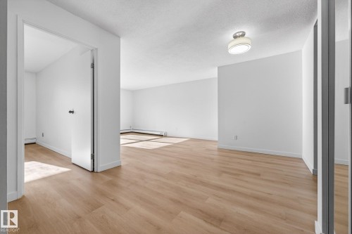 Empty room featuring light wood finished floors, a textured ceiling, and a baseboard radiator - 207 11007 83 Avenue, Edmonton, AB - Indoor Photo Showing Other Room