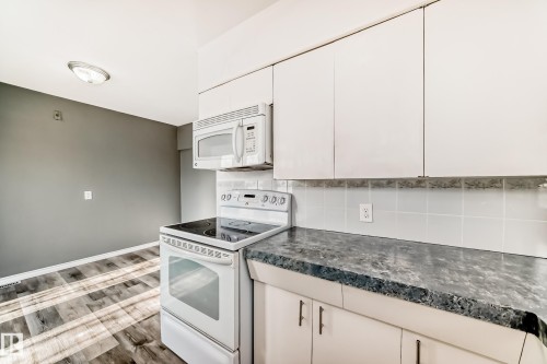Kitchen with white appliances, dark countertops, wood finished floors, white cabinetry, and backsplash - 8639 64 Avenue Nw, Edmonton, AB - Indoor Photo Showing Kitchen