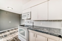 Kitchen with white appliances, dark countertops, wood finished floors, white cabinetry, and backsplash - 