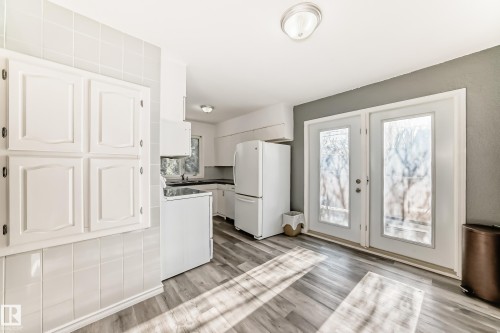 Kitchen with white appliances, white cabinets, dark countertops, and light wood finished floors - 8639 64 Avenue Nw, Edmonton, AB - Indoor Photo Showing Kitchen