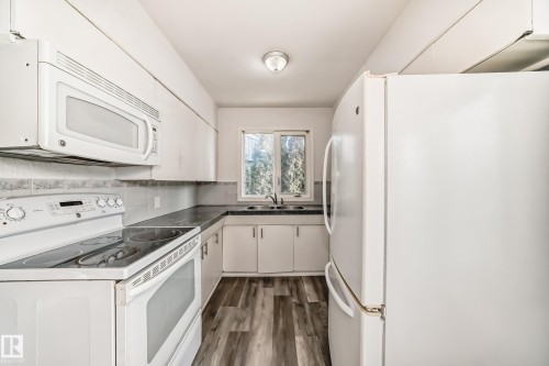 Kitchen with white appliances, white cabinets, dark wood finished floors, and dark countertops - 8639 64 Avenue Nw, Edmonton, AB - Indoor Photo Showing Kitchen With Double Sink
