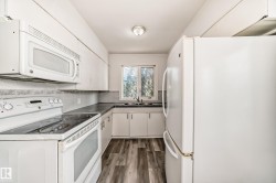 Kitchen with white appliances, white cabinets, dark wood finished floors, and dark countertops - 