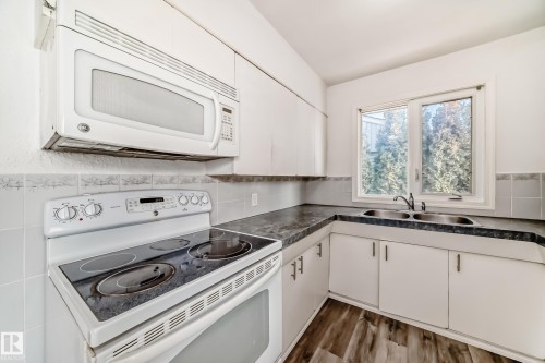 Kitchen featuring white appliances, white cabinets, dark countertops, and wood finished floors - 8639 64 Avenue Nw, Edmonton, AB - Indoor Photo Showing Kitchen With Double Sink