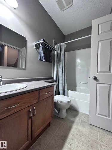 Full bath with vanity, a textured ceiling, shower / bathtub combination with curtain, and light tile patterned floors - 23 4821 Terwillegar Common, Edmonton, AB - Indoor Photo Showing Bathroom