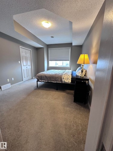 Carpeted bedroom with a textured ceiling and baseboards - 23 4821 Terwillegar Common, Edmonton, AB - Indoor Photo Showing Bedroom