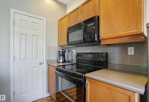 Kitchen featuring black appliances, light countertops, tasteful backsplash, and light wood finished floors - 23 4821 Terwillegar Common, Edmonton, AB - Indoor Photo Showing Kitchen