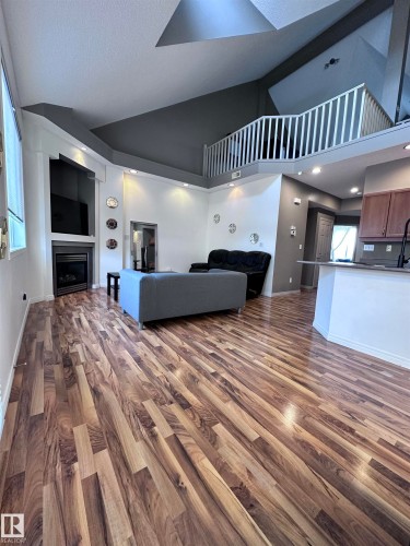 Living area featuring dark wood-style flooring, a fireplace, and vaulted ceiling - 23 4821 Terwillegar Common, Edmonton, AB - Indoor With Fireplace