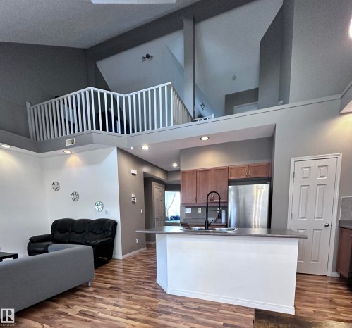 Kitchen with open floor plan, freestanding refrigerator, dark wood-style floors, wood finish cabinets, and an island with sink - 23 4821 Terwillegar Common, Edmonton, AB - Indoor Photo Showing Other Room