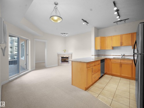 Kitchen with light stone counters, open floor plan, a peninsula, a fireplace, and light carpet - 308 10333 112 Street Street, Edmonton, AB - Indoor Photo Showing Kitchen