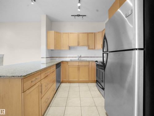 Kitchen featuring stainless steel appliances, light wood finish cabinets, light stone counters, light tile patterned flooring, and a peninsula - 308 10333 112 Street Street, Edmonton, AB - Indoor Photo Showing Kitchen