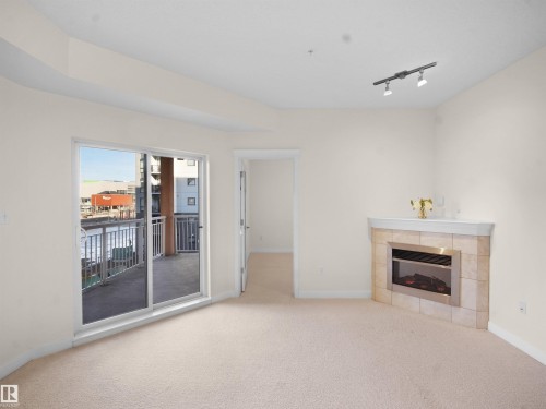 Unfurnished living room with carpet floors, track lighting, and a tiled fireplace - 308 10333 112 Street Street, Edmonton, AB - Indoor Photo Showing Other Room With Fireplace
