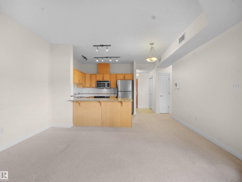 Kitchen featuring light carpet, a peninsula, a kitchen bar, open floor plan, and stainless steel microwave - 308 10333 112 Street Street, Edmonton, AB - Indoor Photo Showing Kitchen