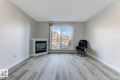 Unfurnished room featuring light wood-style flooring and a glass covered fireplace - 237 17447 98A Avenue, Edmonton, AB - Indoor Photo Showing Living Room With Fireplace
