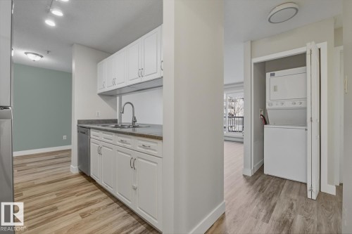 Kitchen with white cabinets, light wood-type flooring, stacked washer / drying machine, and stainless steel appliances - 237 17447 98A Avenue, Edmonton, AB - Indoor