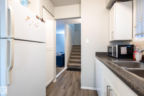 Kitchen featuring white appliances, white cabinets, dark countertops, and dark wood finished floors - 3530 42 Street, Edmonton, AB - Indoor Photo Showing Kitchen With Double Sink