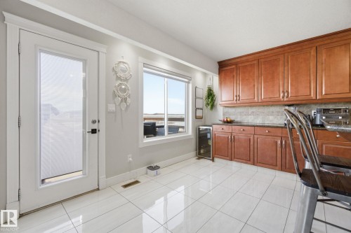 Kitchen featuring wood finish cabinetry, wine cooler, tasteful backsplash, light tile patterned floors, and dark stone countertops - 48 Douglas Crescent, Leduc, AB - Indoor