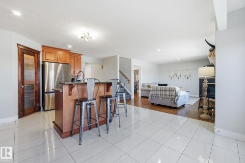 Kitchen with a kitchen bar, freestanding refrigerator, light tile patterned floors, wood finish cabinetry, and an island with sink - 48 Douglas Crescent, Leduc, AB - Indoor