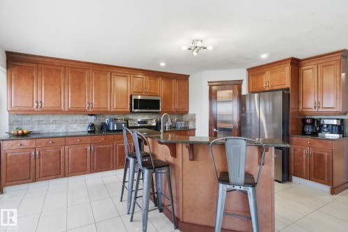Kitchen featuring wood finish cabinetry, a kitchen breakfast bar, stainless steel appliances, a kitchen island with sink, and dark stone counters - 48 Douglas Crescent, Leduc, AB - Indoor Photo Showing Kitchen