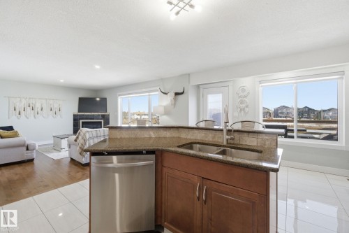 Kitchen featuring light tile patterned flooring, an island with sink, stainless steel dishwasher, dark stone countertops, and open floor plan - 48 Douglas Crescent, Leduc, AB - Indoor Photo Showing Kitchen With Double Sink
