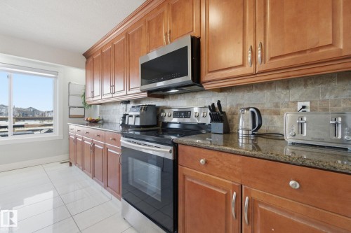 Kitchen featuring stainless steel appliances, dark stone counters, wood finish cabinetry, light tile patterned flooring, and decorative backsplash - 48 Douglas Crescent, Leduc, AB - Indoor Photo Showing Kitchen