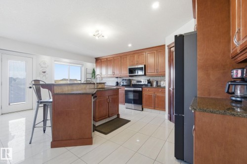 Kitchen featuring a kitchen bar, wood finish cabinetry, stainless steel appliances, an island with sink, and dark stone counters - 48 Douglas Crescent, Leduc, AB - Indoor Photo Showing Kitchen
