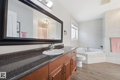 Bathroom featuring light wood finished floors, vanity, a garden tub, a shower with shower curtain, and tile walls - 48 Douglas Crescent, Leduc, AB - Indoor Photo Showing Bathroom