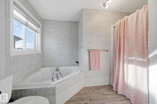 Bathroom featuring tile walls, a garden tub, curtained shower, and light wood finished floors - 48 Douglas Crescent, Leduc, AB - Indoor Photo Showing Bathroom