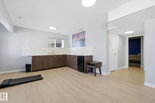 Bar area with dark wood finish cabinetry, light wood-style floors, decorative backsplash, black refrigerator, and modern cabinets - 48 Douglas Crescent, Leduc, AB - Indoor Photo Showing Kitchen