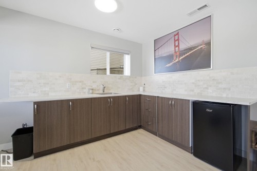 Kitchen featuring black refrigerator, light wood-style flooring, dark wood finish cabinets, light stone counters, and modern cabinets - 48 Douglas Crescent, Leduc, AB - Indoor