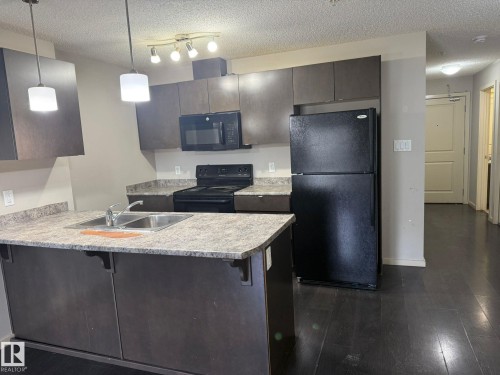 Kitchen with a breakfast bar area, black appliances, a textured ceiling, light countertops, and dark wood finished floors - 211 340 Windermere Road, Edmonton, AB - Indoor Photo Showing Kitchen With Double Sink