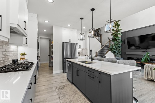 Kitchen featuring a breakfast bar, two tone cabinets, decorative light fixtures, an island with sink, and decorative backsplash - 5 Starling, Fort Saskatchewan, AB 