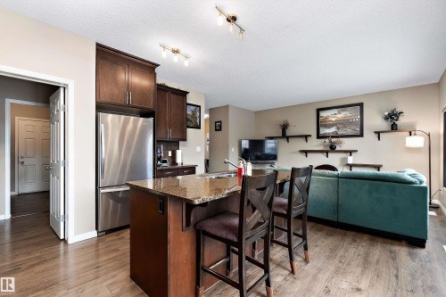 Kitchen with dark wood finish cabinetry, freestanding refrigerator, a breakfast bar area, open floor plan, and an island with sink - 33 Sutherland Street, Leduc, AB - Indoor Photo Showing Kitchen
