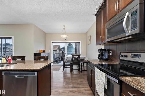 Kitchen with stainless steel appliances, dark wood finish cabinets, dark stone countertops, dark wood-type flooring, and a textured ceiling - 33 Sutherland Street, Leduc, AB - Indoor Photo Showing Kitchen
