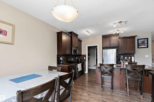Kitchen featuring dark wood finish cabinets, a kitchen breakfast bar, stainless steel appliances, backsplash, and dark wood-type flooring - 33 Sutherland Street, Leduc, AB - Indoor