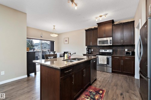 Kitchen with dark wood finish cabinetry, stainless steel appliances, an island with sink, decorative backsplash, and dark stone countertops - 33 Sutherland Street, Leduc, AB - Indoor Photo Showing Kitchen With Double Sink