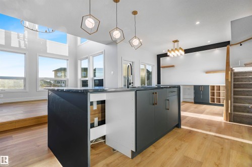 Kitchen with modern cabinets, hanging lights, an island with sink, light wood-style flooring, and dark countertops - 366 Creekside Green, Leduc, AB - Indoor Photo Showing Kitchen