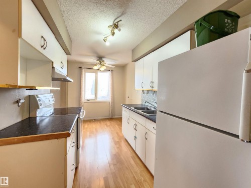 Kitchen featuring white appliances, dark countertops, a ceiling fan, a textured ceiling, and light wood-style floors - 6 14320 80 Street, Edmonton, AB - Indoor Photo Showing Kitchen With Double Sink