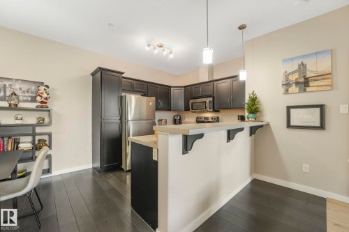 Kitchen with hanging light fixtures, a peninsula, light countertops, stainless steel appliances, and a breakfast bar area - 122 304 Ambleside Link Link, Edmonton, AB - Indoor Photo Showing Kitchen