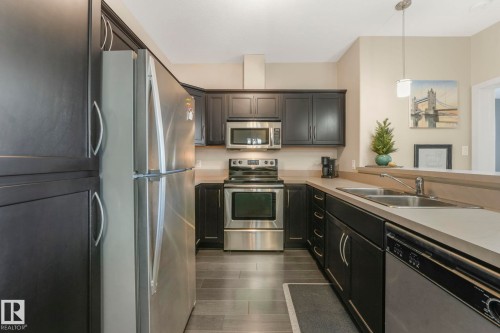 Kitchen featuring stainless steel appliances, light countertops, pendant lighting, and dark wood-style floors - 122 304 Ambleside Link Link, Edmonton, AB - Indoor Photo Showing Kitchen With Double Sink