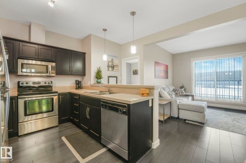 Kitchen featuring stainless steel appliances, light countertops, decorative light fixtures, a peninsula, and open floor plan - 122 304 Ambleside Link Link, Edmonton, AB - Indoor Photo Showing Kitchen With Double Sink