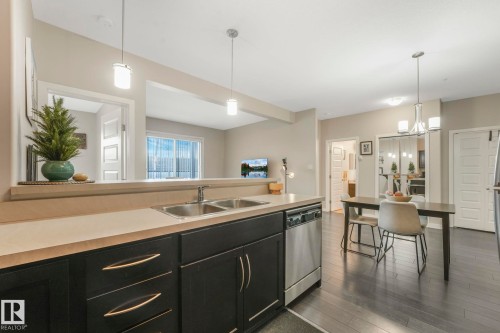 Kitchen featuring dark cabinetry, light countertops, stainless steel dishwasher, and dark wood-style flooring - 122 304 Ambleside Link Link, Edmonton, AB - Indoor Photo Showing Kitchen With Double Sink